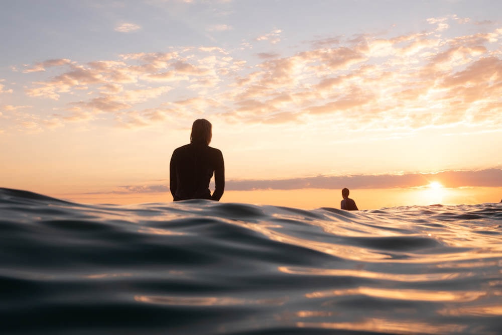Surfers waiting for waves in the ocean during a colorful sunset