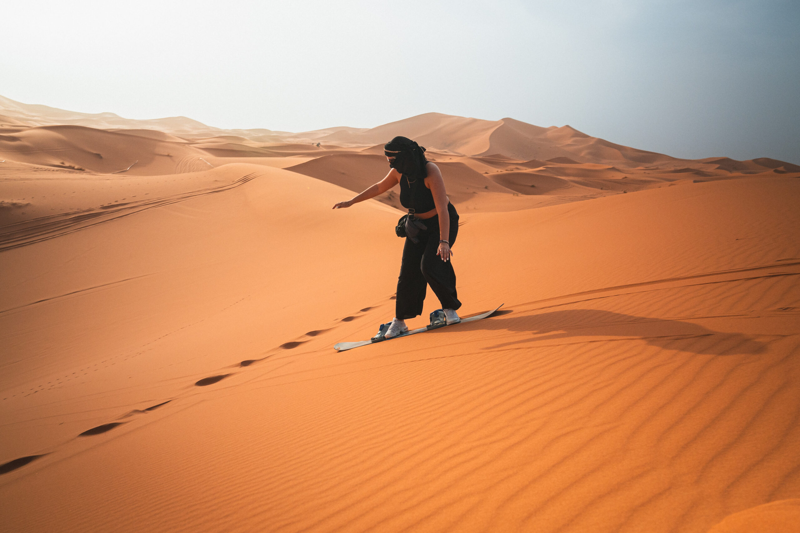 Traveler sandboarding down the golden dunes of the Sahara Desert in Morocco