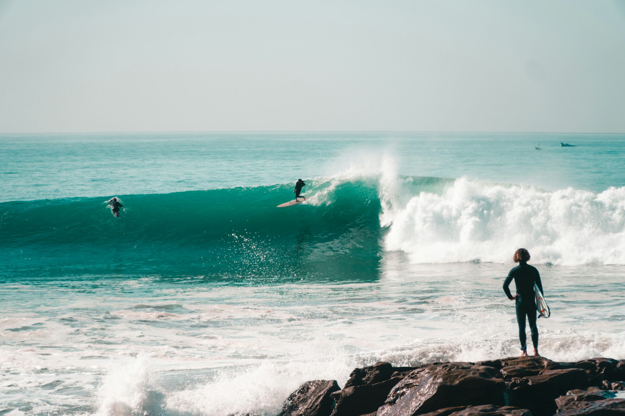 Surfer riding a large, powerful turquoise point break wave in winter, Tamraght surf spot.