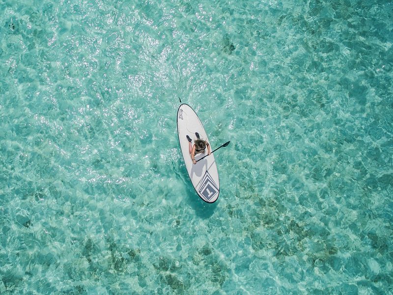 Surfer paddling alone in crystal-clear turquoise water