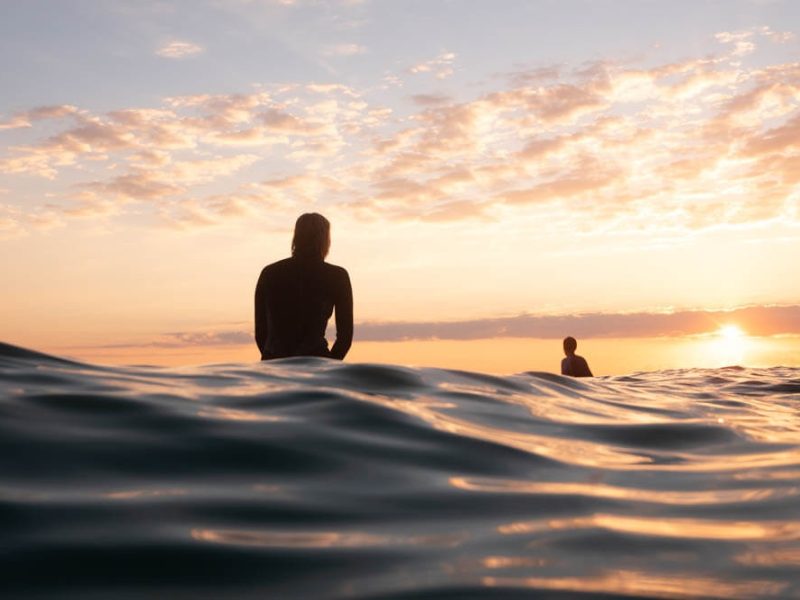 Surfers waiting for waves in the ocean during a colorful sunset